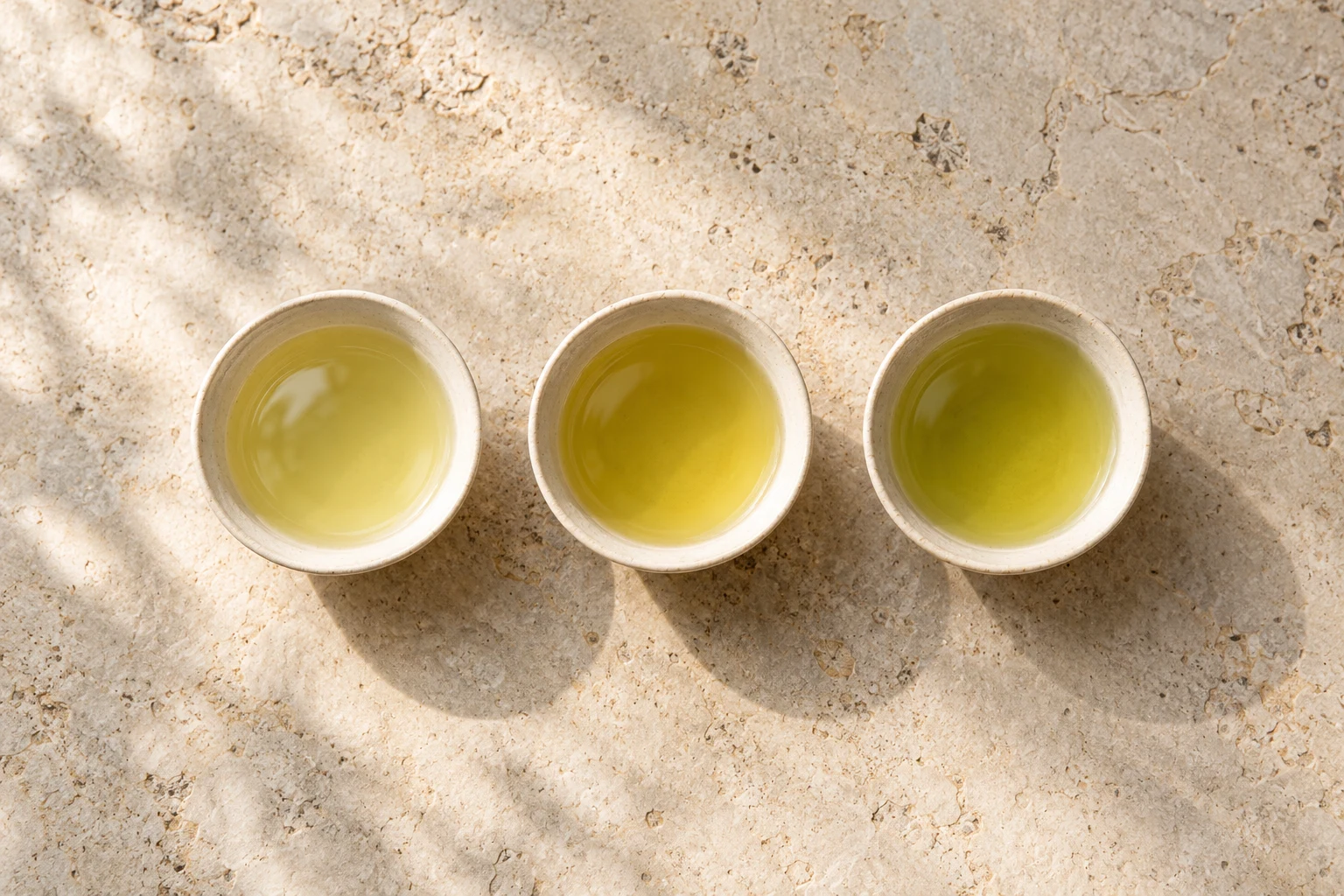 Three small cups of pale golden-green tea on light stone, an illustrative still life